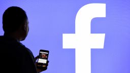 15 March 2019, Schleswig-Holstein, Aukrug-Homfeld: ILLUSTRATION - A man with a smartphone stands in front of a monitor with the Facebook logo. Photo: Carsten Rehder/dpa (Photo by Carsten Rehder/picture alliance via Getty Images)