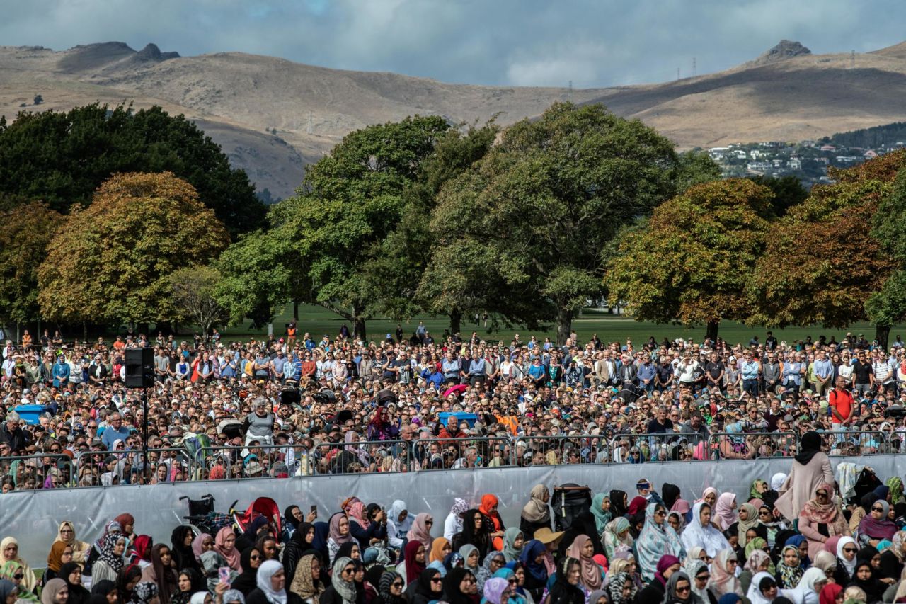 Visitors look on as Muslims attend Friday prayers in a park near Al Noor mosque.