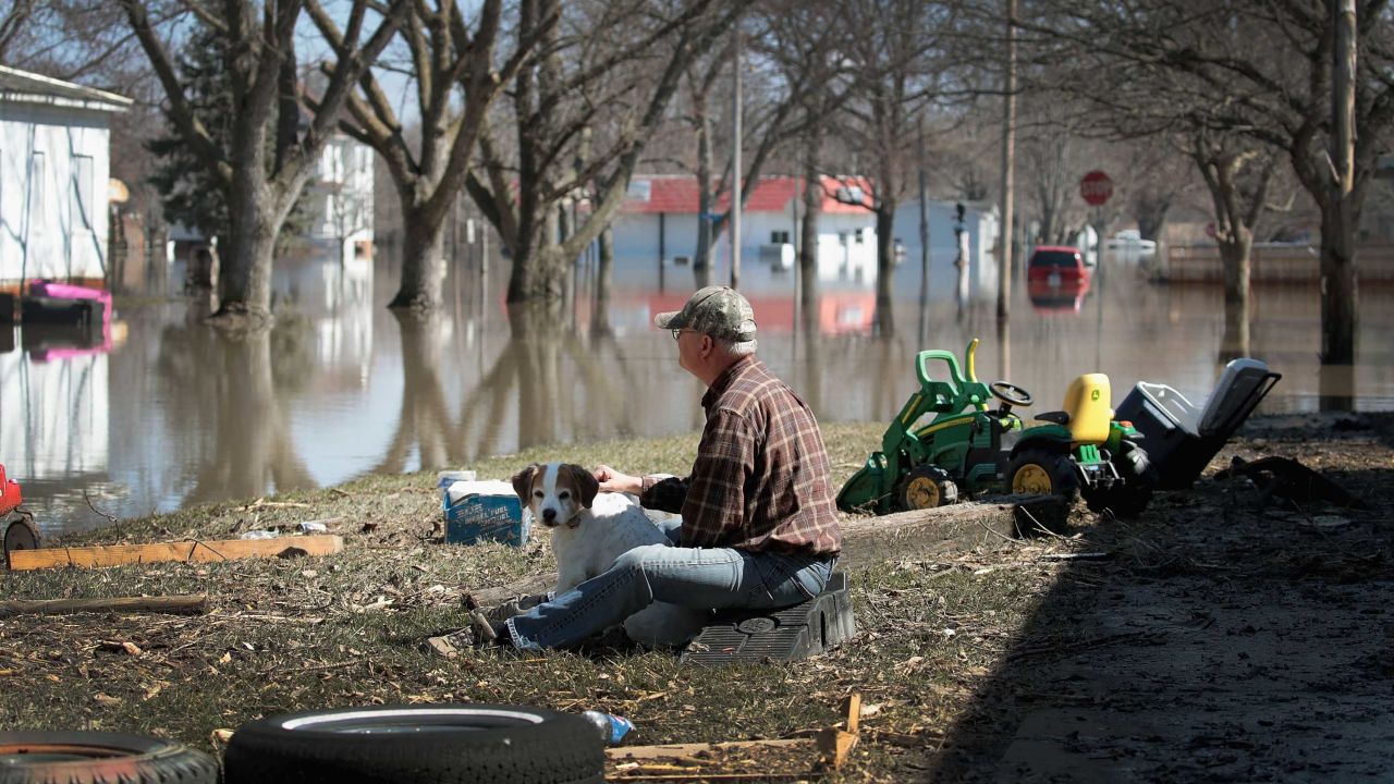 Dave Mincer sits along a flooded street with a friend's dog in Hamburg, Iowa, on Wednesday, March 20.