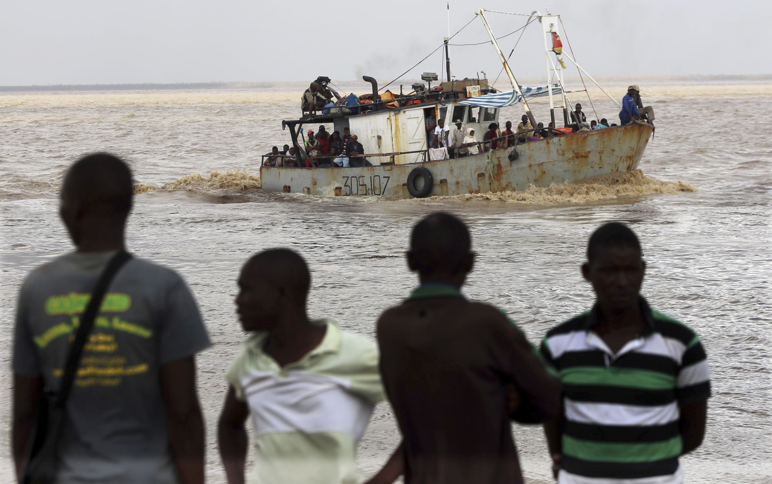 Men watch the arrival of a boat carrying displaced families rescued from a flooded area of Mozambique's Buzi district on March 23.