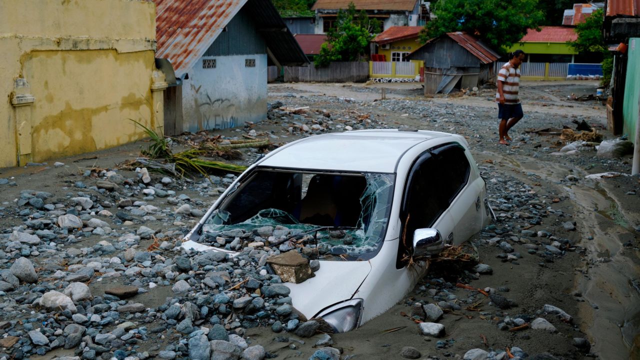 A car sits abandoned in the mud on a flooded street.