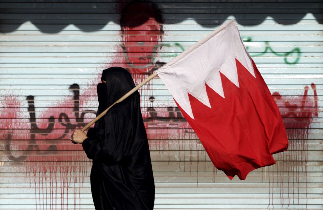 A Bahraini anti-government protester carries the national flag past anti-government graffiti sprayed over by authorities in 2013. 