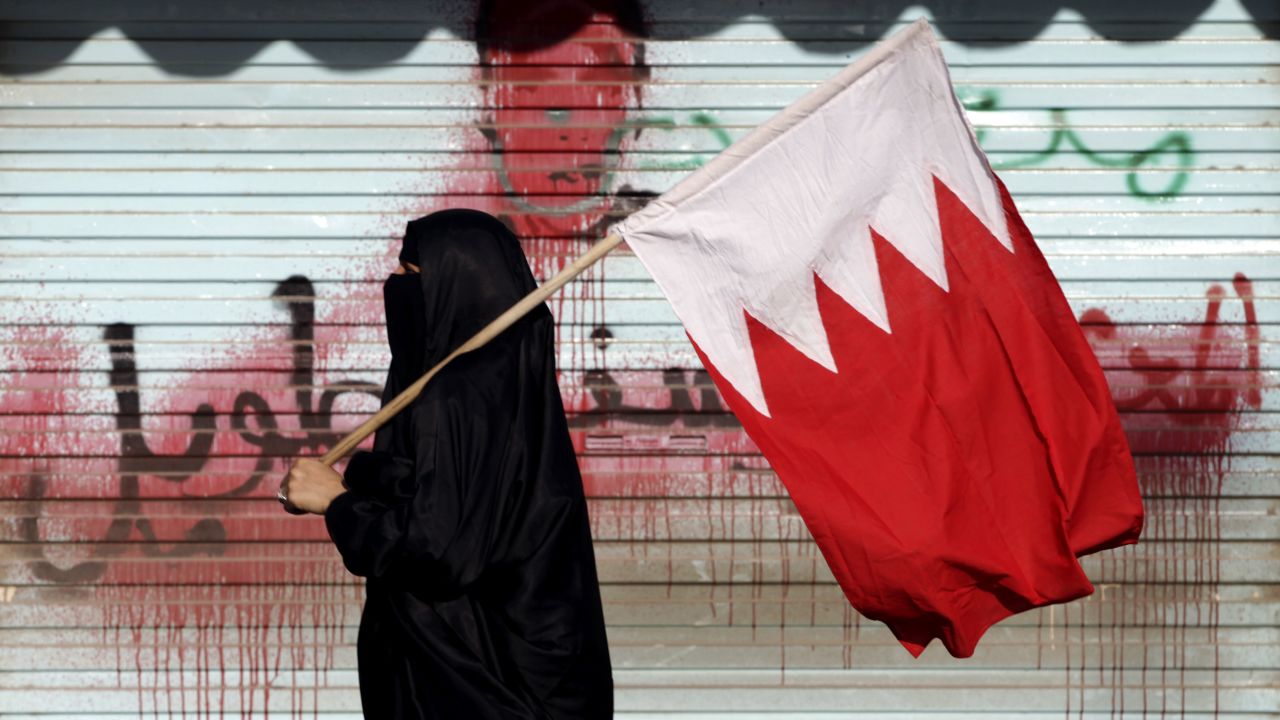 A Bahraini anti-government protester carries the national flag past anti-government graffiti sprayed over by authorities in 2013.