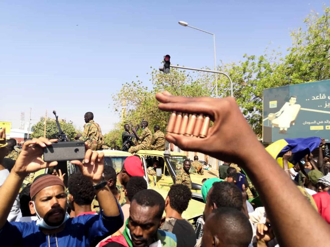 A protester holds bullet cartridges as others gather in front of security forces Monday outside the military headquarters.