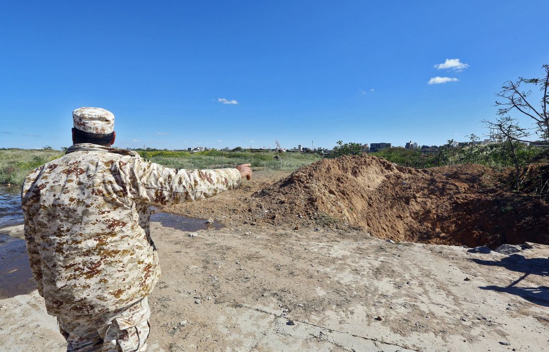 A member of the Libyan security forces points towards a crater on the ground following an air strike at Mitiga International Airport in the capital Tripoli on April 8, 2019. 