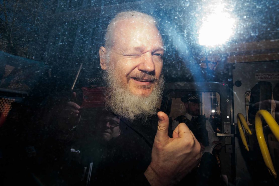 Julian Assange gestures to the media from a police vehicle.