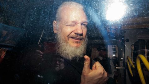 Julian Assange gestures to the media from a police vehicle.