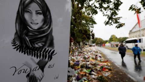 People walk past flowers and tributes displayed in memory of the twin mosque massacre victims outside the Botanical Gardens in Christchurch on April 5, 2019.