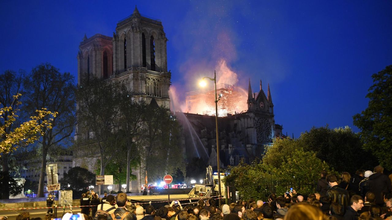 Crowds look on as flames and smoke billow from the roof at Notre-Dame Cathedral in Paris on April 15, 2019. - A fire broke out at the landmark Notre-Dame Cathedral in central Paris, potentially involving renovation works being carried out at the site, the fire service said.Images posted on social media showed flames and huge clouds of smoke billowing above the roof of the gothic cathedral, the most visited historic monument in Europe. (Photo by ERIC FEFERBERG / AFP)