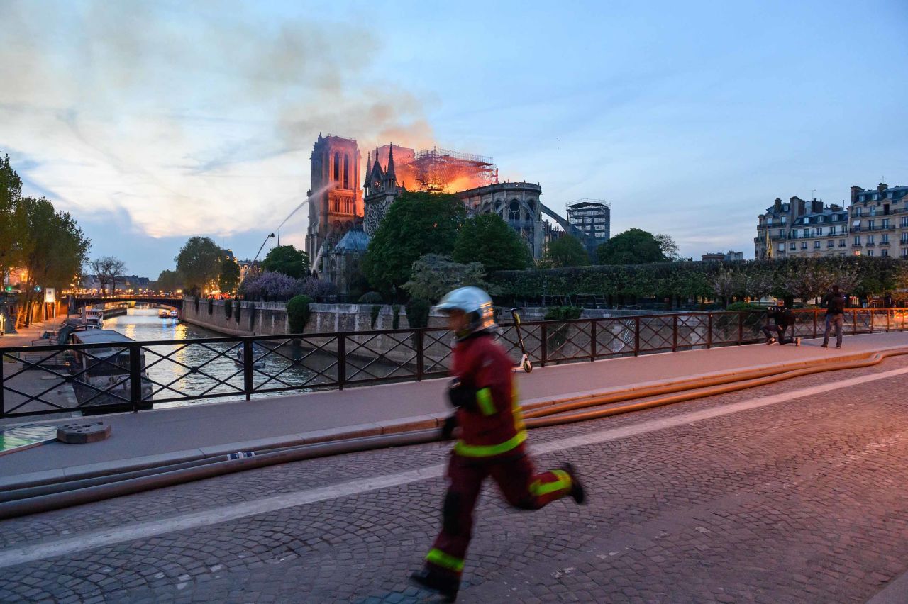 Flames and smoke rise from Notre Dame as a firefighter rushes past.