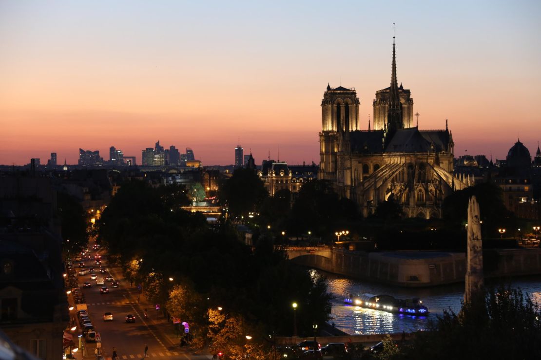 A 2015 photograph shows the Notre Dame Cathedral at sunset. La Défense business district is pictured in the background.