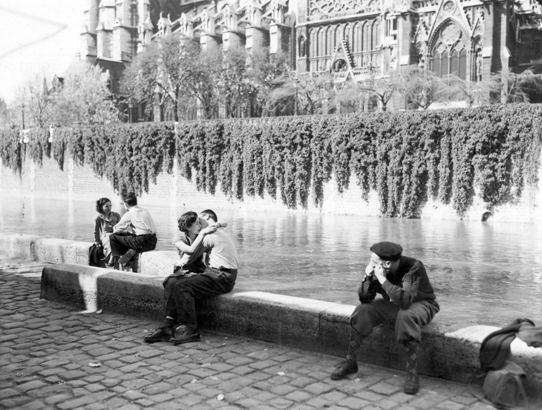 Couples kiss and chat by the Seine River close to Notre Dame Cathedral in the 1950s.