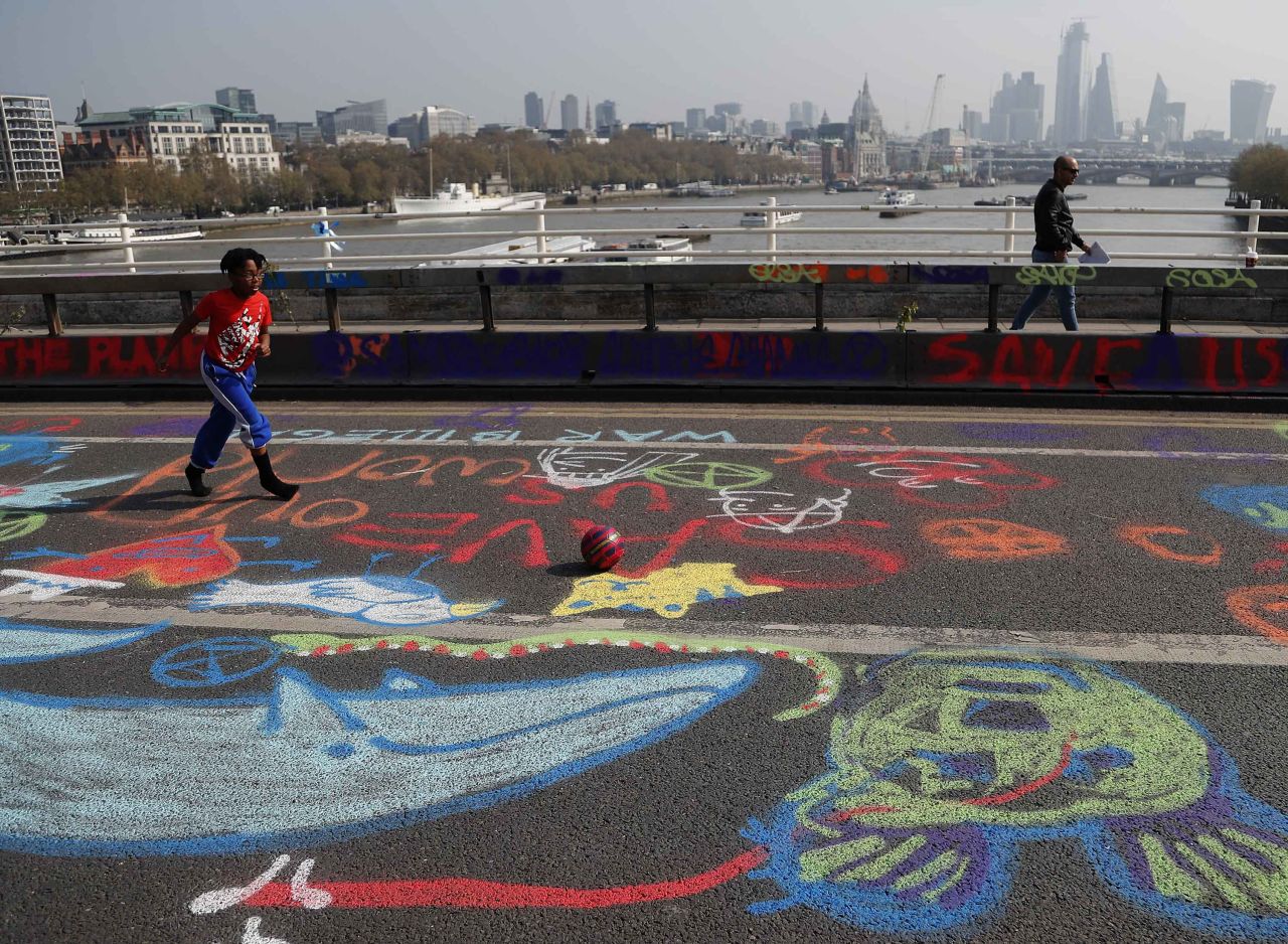 A boy plays football across chalk drawings during the ongoing blockade of Waterloo Bridge.