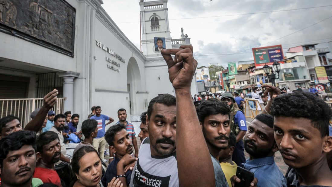 A man holds up a blood-stained photograph as people wait to identify the bodies of their loved ones in front of St. Anthony's Church.