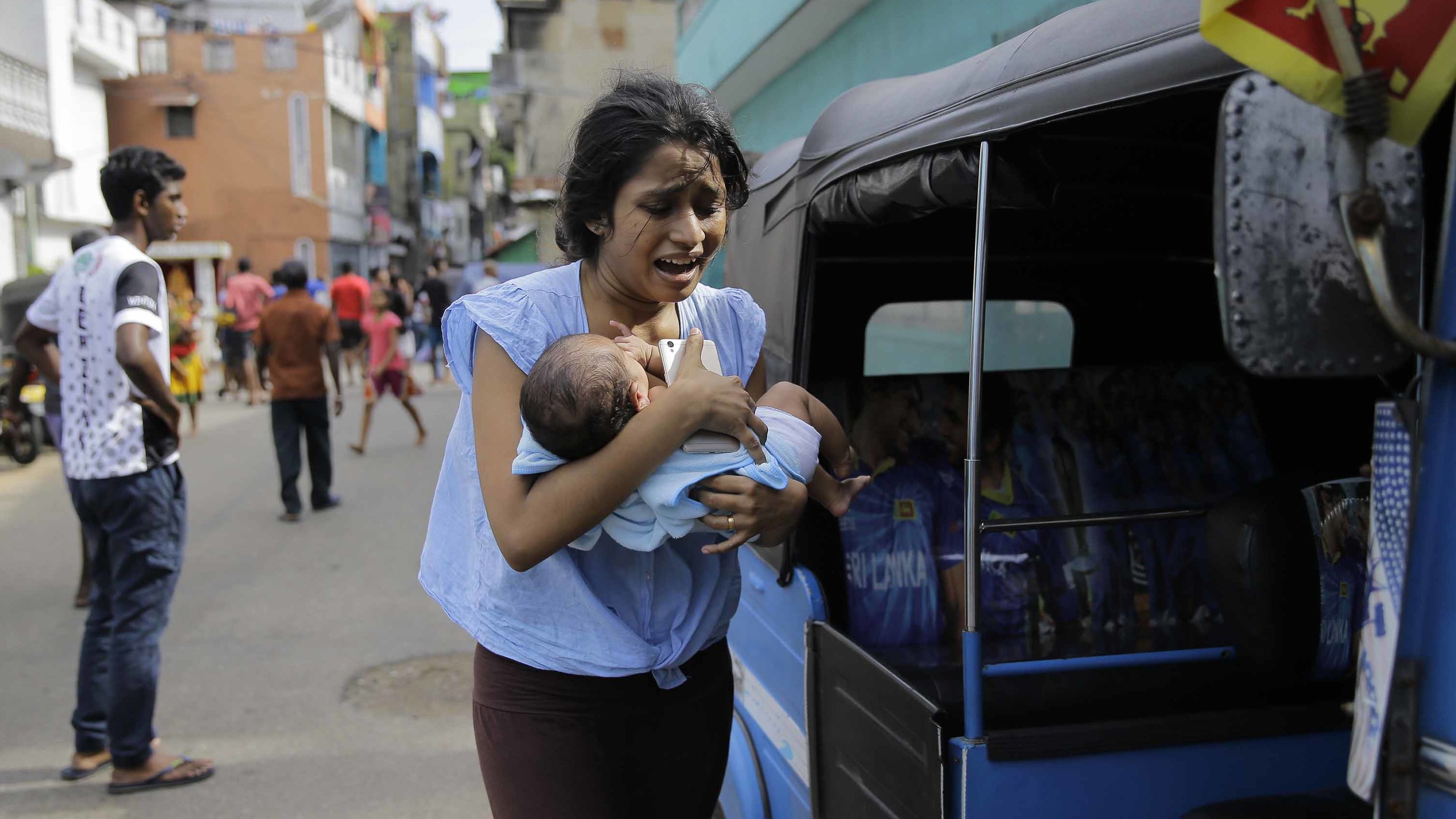 A woman carrying an infant runs for safety after police found a suspicious vehicle parked in Colombo, Sri Lanka, on Monday, April 22, a day after several coordinated bombings across the country killed hundreds.