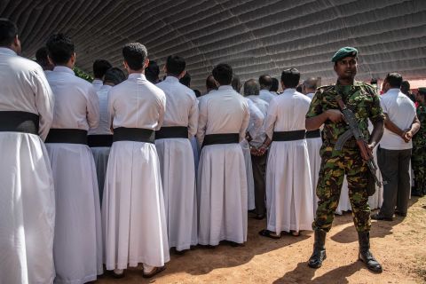 A soldier stands guard next to members of the clergy during a mass funeral in Negombo on Tuesday.