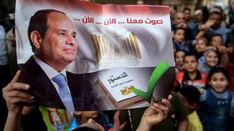 An Egyptian man outside a polling station holds a banner reading: "Vote with us... now... now."