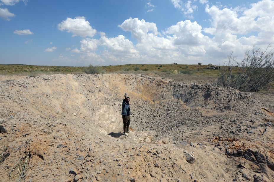 A fighter loyal to Libya's Government of National Accord waves from a crater reportedly caused by an airstrike west of the city of Aziziyah, southwest  of Tripoli, on April 14.