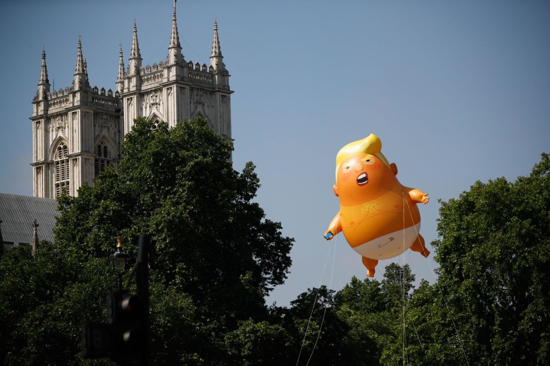 Pedestrians walk past as a giant balloon depicting US President Donald Trump as an orange baby floats next to the towers of Westminster Abbey during a demonstration against Trump's visit to the UK in Parliament Square in London on July 13, 2018. 