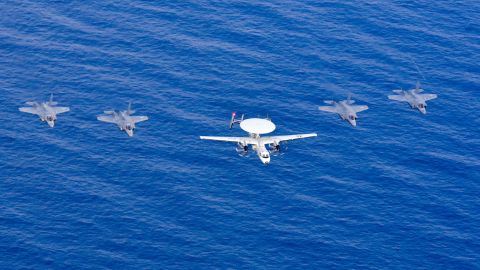 A US Navy carrier-based E-2D Hawkeye airborne radar plane and four US Marine Corps F-35B Lightning jets fly over the South China Sea.