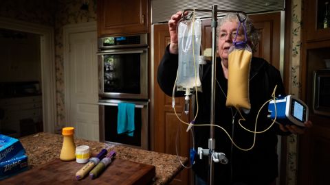 Dafoe prepares an IV bag and feeding tubes in their home's kitchen.