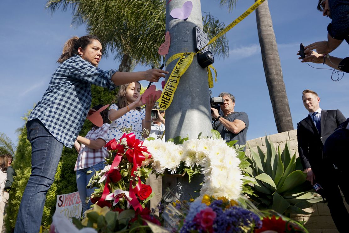 A woman and a young girl place notes on a light post near flowers across the street from the Chabad of Poway Synagogue.