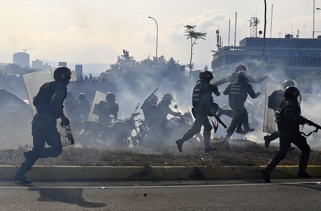Military members loyal to Maduro run under a cloud of tear gas after being repelled with rifle fire from pro-Guaido military members on April 30.
