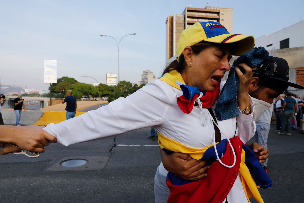 A woman affected by tear gas is aided by fellow opponents of Maduro.