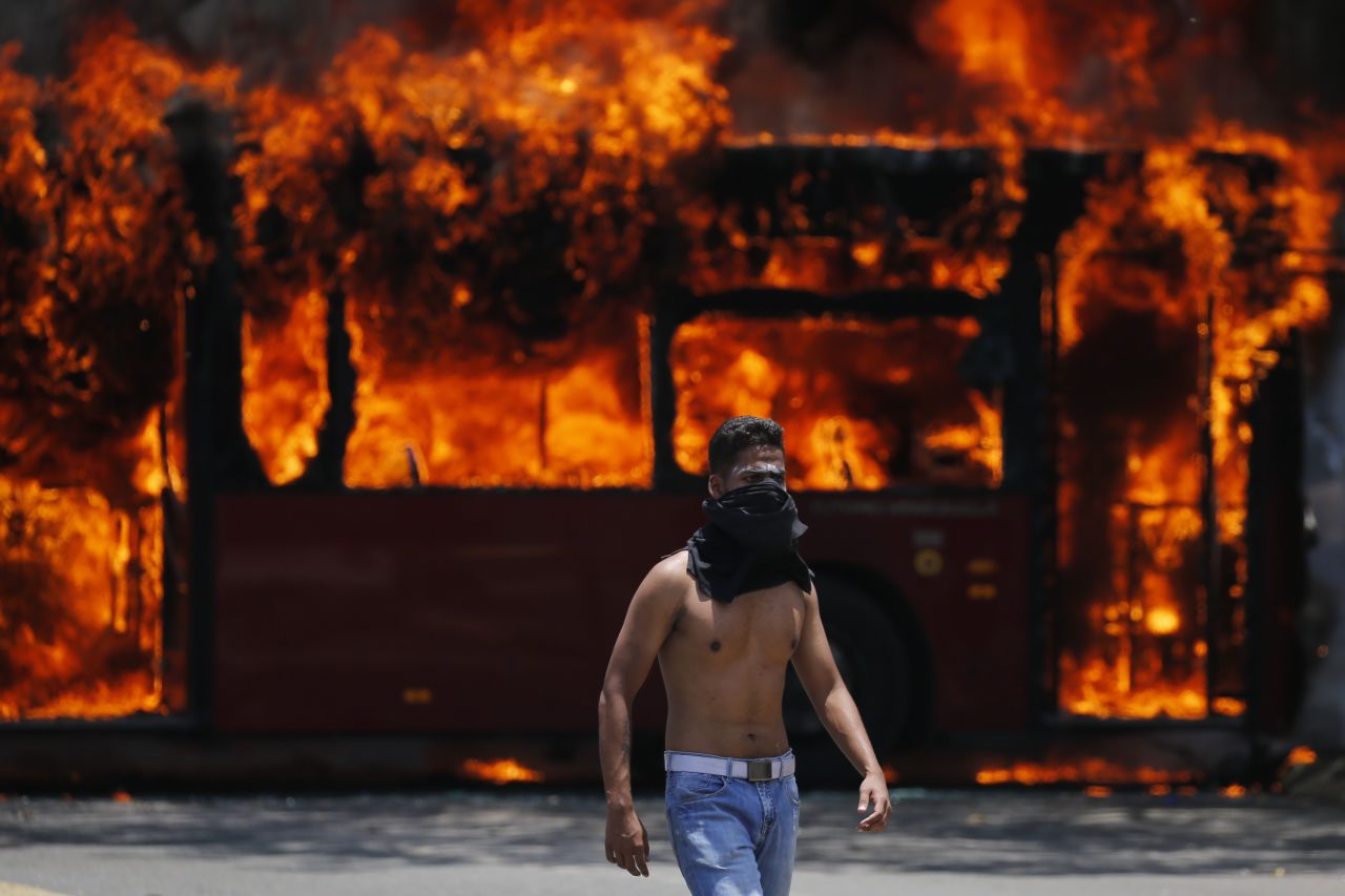 An anti-government protester walks near a bus that was set on fire by Maduro opponents on April 30.