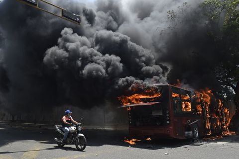 An opposition demonstrator passes by a government bus that was set on fire during clashes on April 30.