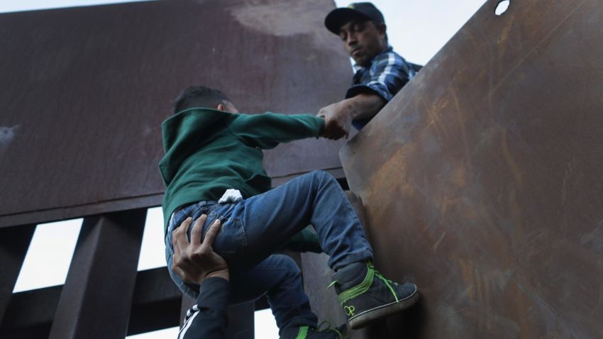 TIJUANA, MEXICO - DECEMBER 02:  A boy is hoisted by fellow members of the migrant caravan over the U.S.-Mexico border fence on December 2, 2018 from Tijuana, Mexico. Numerous members of the caravan were able to cross over from Tijuana to San Diego and were quickly taken into custody by U.S. Border Patrol agents. Most had planned to request political asylum in the United States after traveling more than 6 weeks from Central America.  (Photo by John Moore/Getty Images)