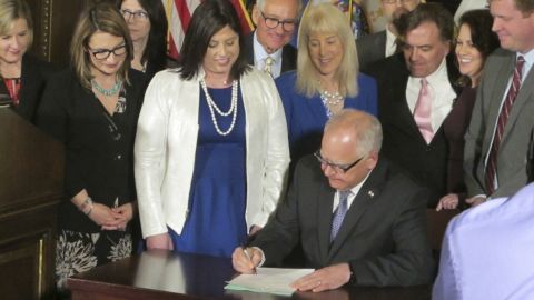 Jenny Teeson, center, in white, looks on as Minnesota Gov. Tim Walz signs a bill repealing a law that prevented prosecutors from filing sexual assault charges against people accused of raping their spouse.