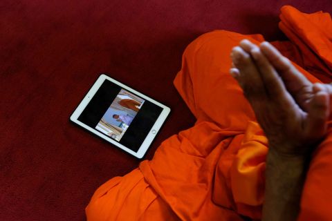 A tablet displaying King Maha Vajiralongkorn undergoing a royal purification ritual is seen as a Buddhist monk prays during the King's coronation on Saturday.