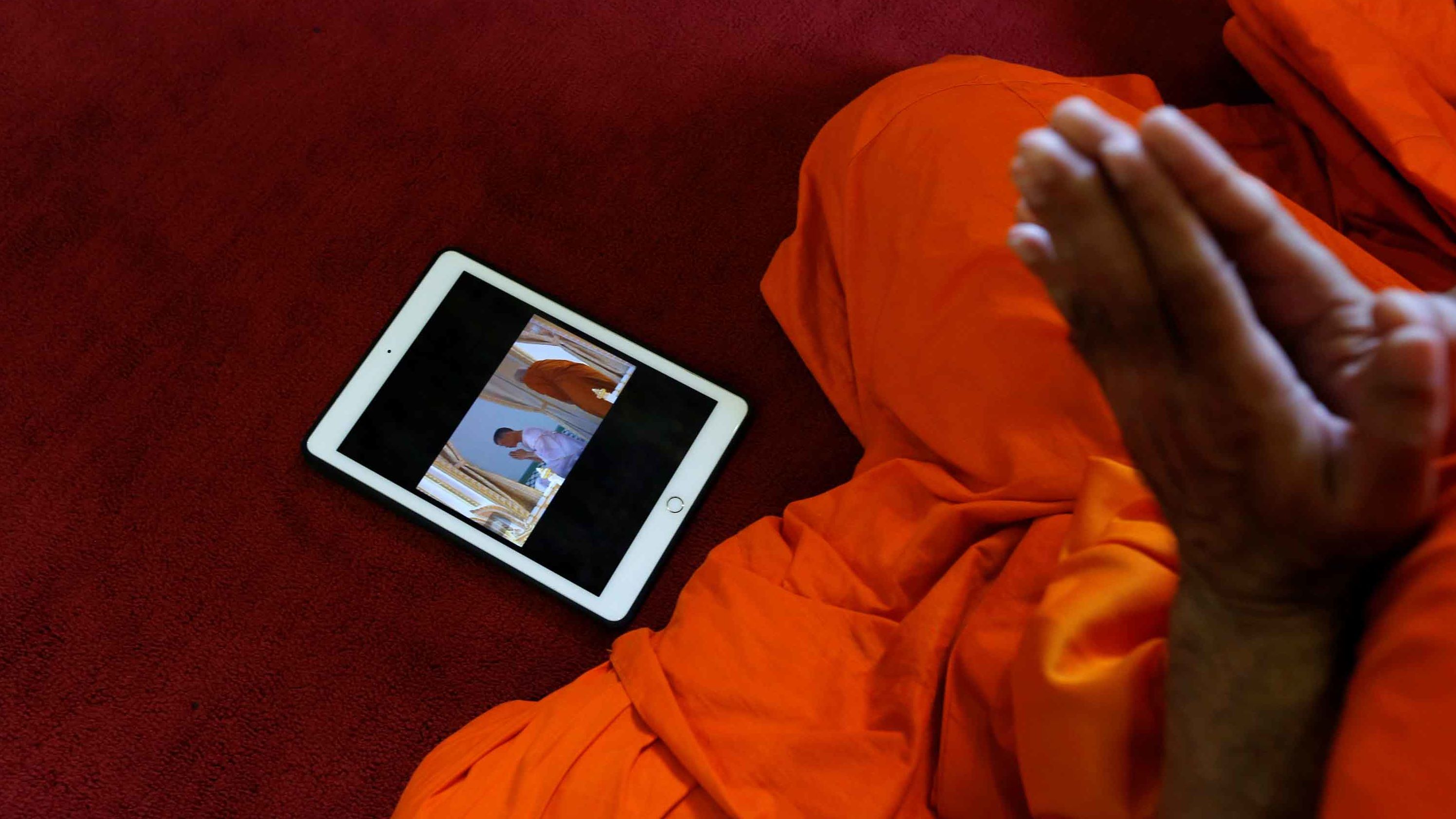 A tablet displaying King Maha Vajiralongkorn undergoing a royal purification ritual is seen as a Buddhist monk prays during the King's coronation on Saturday.