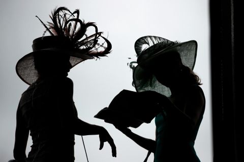 Women wearing extravagant hats read a pamphlet before the Kentucky Derby.