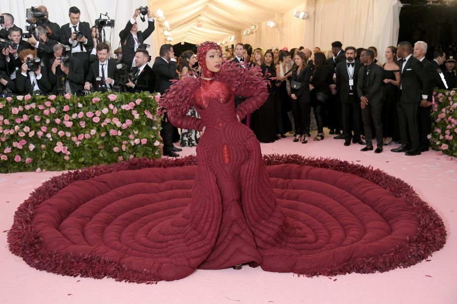 Rapper Cardi B showed up to the Met Gala in a dramatic burgundy gown that extended into a full quilted circular train. The dress, which is trimmed in feathers, was designed by Thom Browne. She also has a matching headpiece on to complete the head-to-toe scarlet look. The dress was decorated with 30,000 feathers, and took 35 people more than 2,000 hours to make.