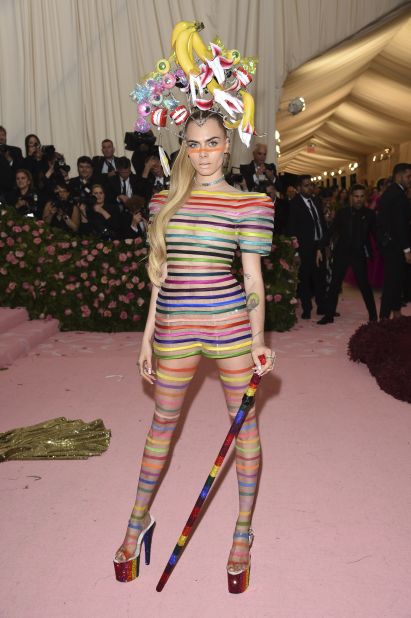 Cara Delevingne arrived in an eye-catching rainbow dress and outlandish headpiece by Dior Haute Couture.