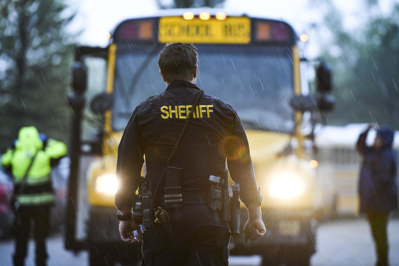 A sheriff's officer watches as students get off buses after being evacuated to a recreation center.