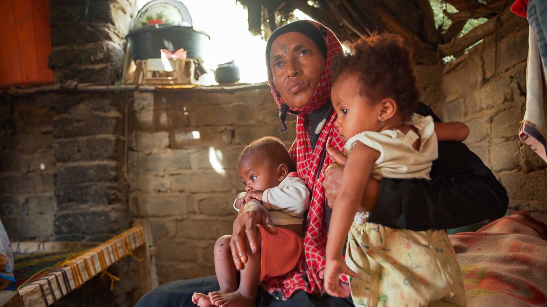 Issham Beshir sits on her mother's lap with her younger brother inside their hut in the village of Bani Qais.