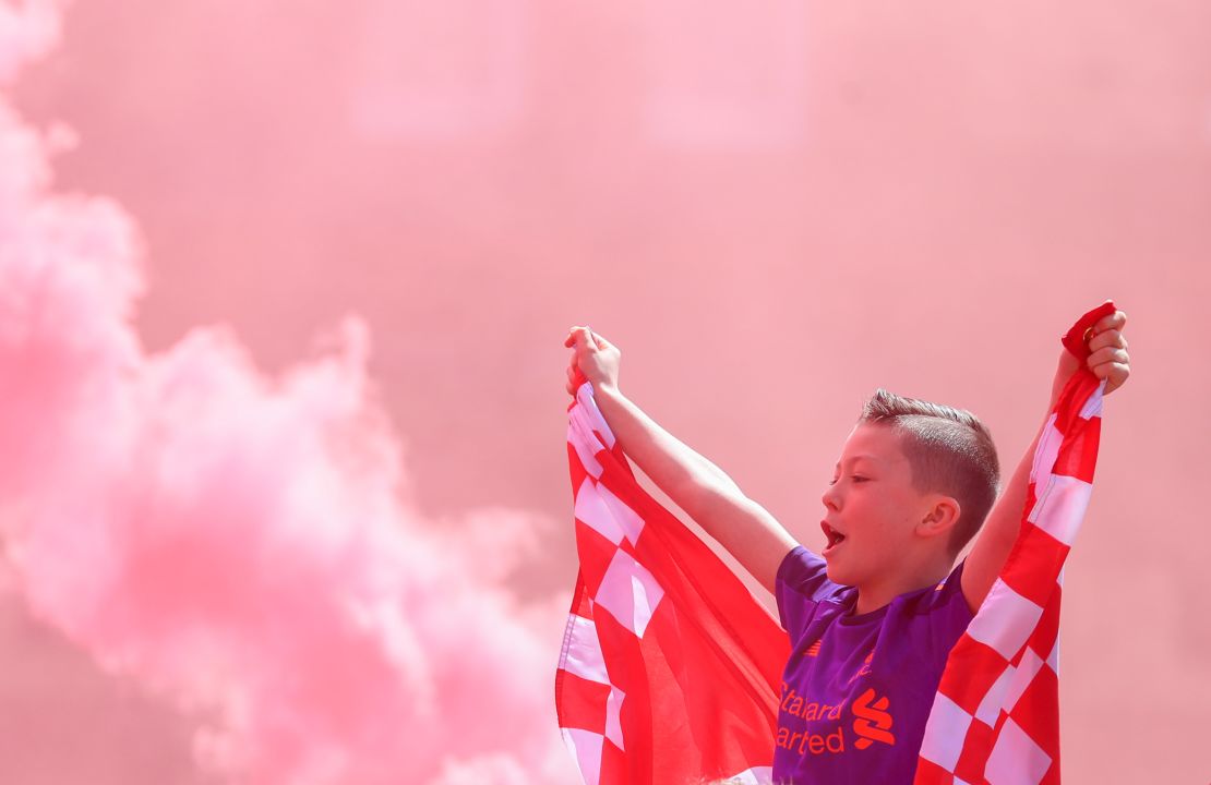 A young Liverpool fan cheers outside Anfield as flares are set off ahead of their team's final match of the season.