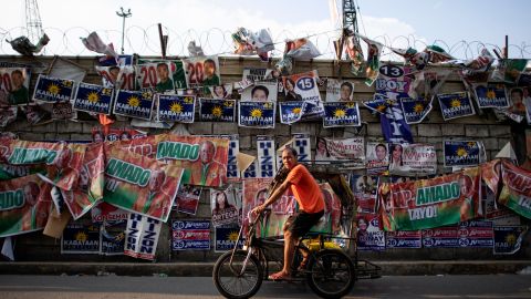A rickshaw driver passes campaign posters in front of Baseco Elementary School in Manila on May 13, 2019.