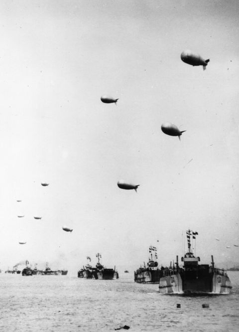Tank landing ships, each towing a protective barrage balloon, leave the English coast carrying supplies to the French beachhead.
