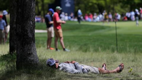 A spectator rests in the shade of a tree along the seventh fairway during the third round.