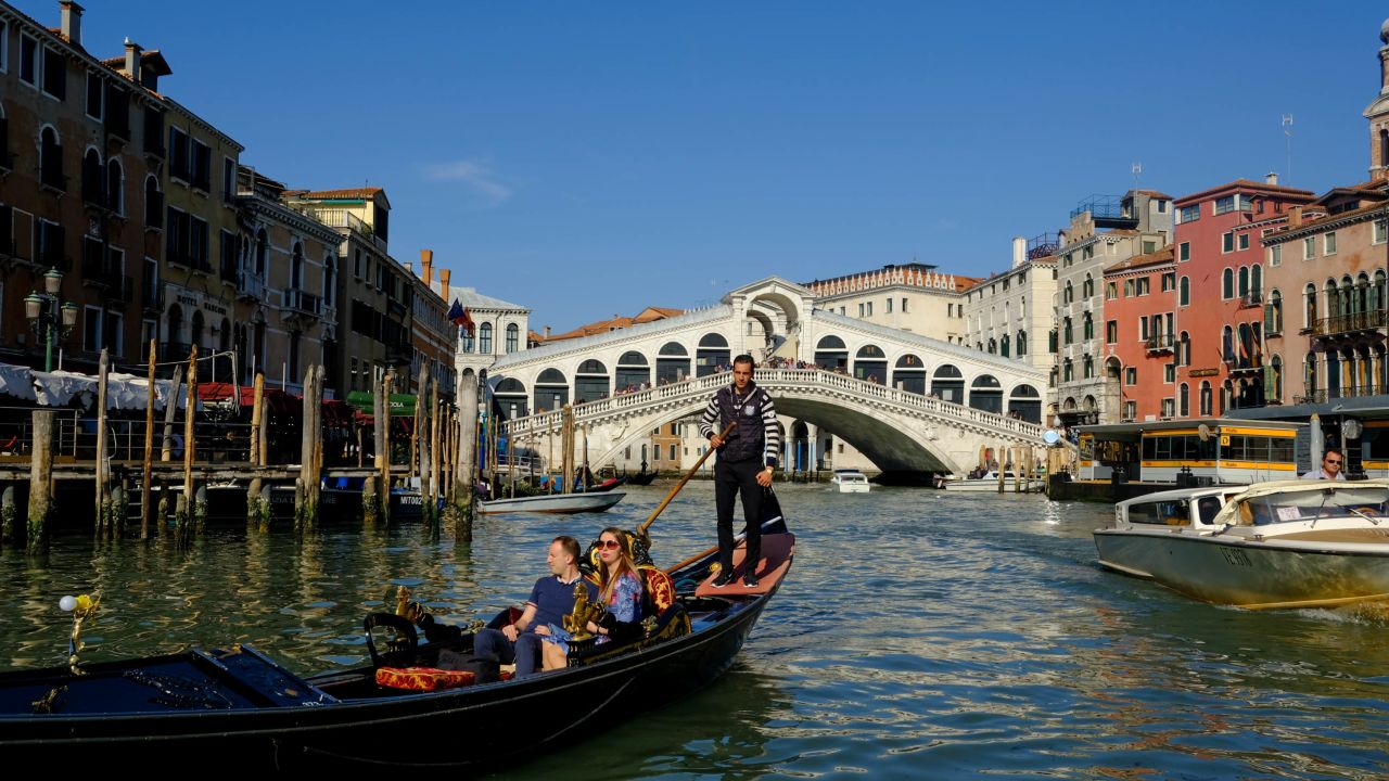 A gondolier glides past the Rialto Bridge, crossing the Grand Canal. 