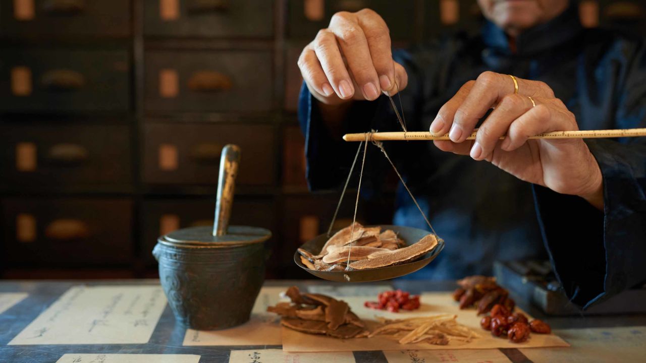 Man measuring ingredients in traditional Asian apothecary. 
