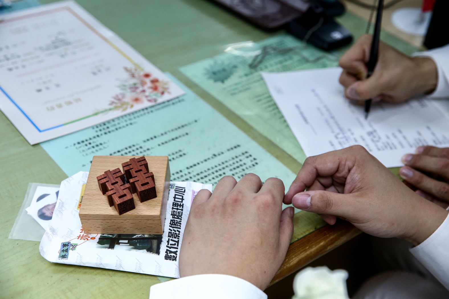 A same-sex couple brings a wooden stamp to their marriage registration. The Chinese characters symbolize the common word for wedding.