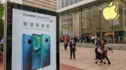People walk past a billboard of the Huawei Mate 20 smartphone in front of an Apple store in Shanghai, China. 