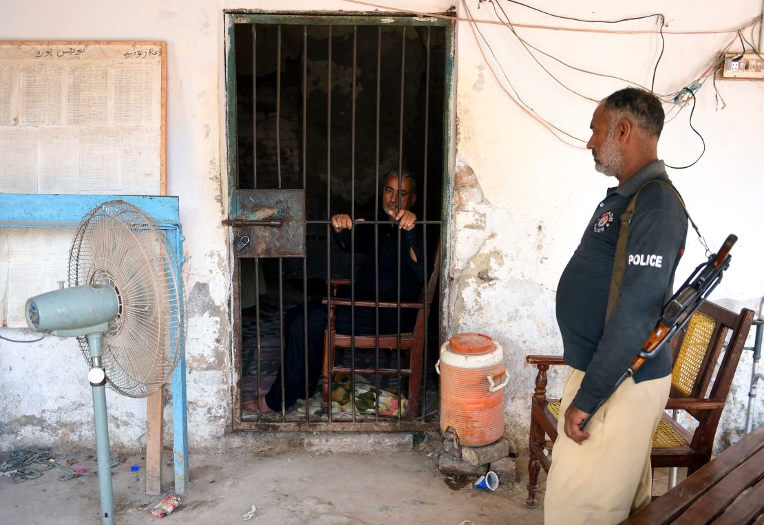 Muzaffar Ghanghro, a Pakistani pediatrician alleged to have been responsible for the HIV outbreak, sits behind bars as a policeman looks on at a local police station in Rato Dero in southern Sindh province on May 9, 2019. 