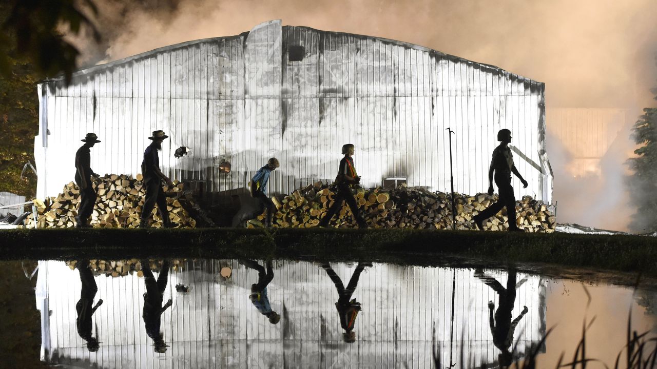 Amish farmers walk around the side of a building as firefighters battle a barn fire in Strasburg Township, Pennsylvania, on Wednesday, May 29.