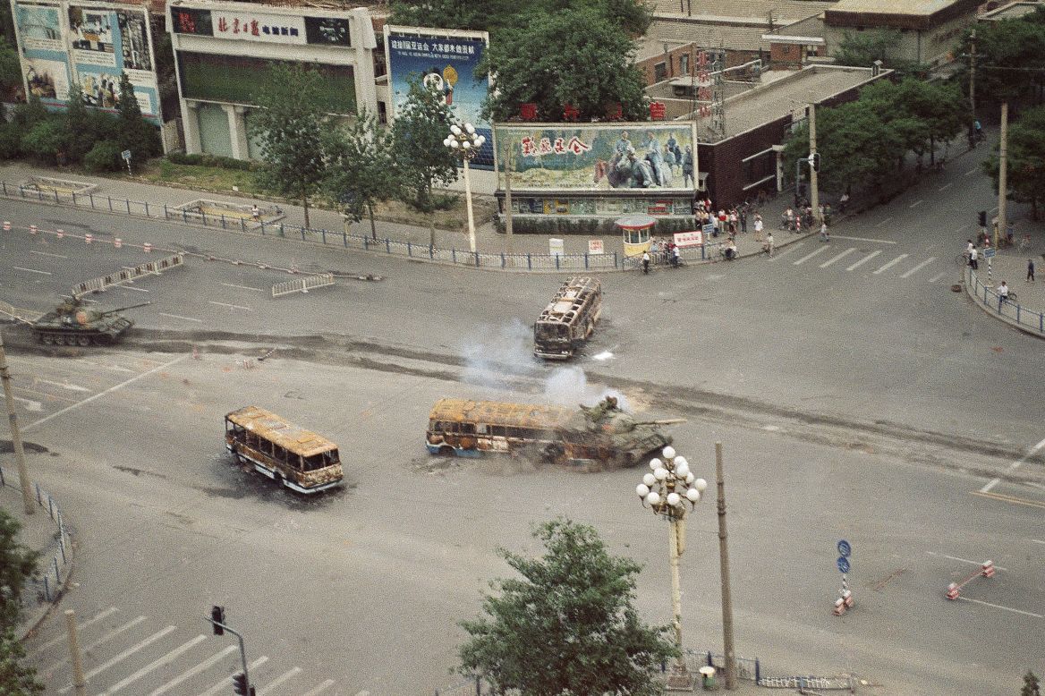 A Chinese army tank crashes through a barricade of burned buses in front of the Beijing Hotel on June 6, 1989.